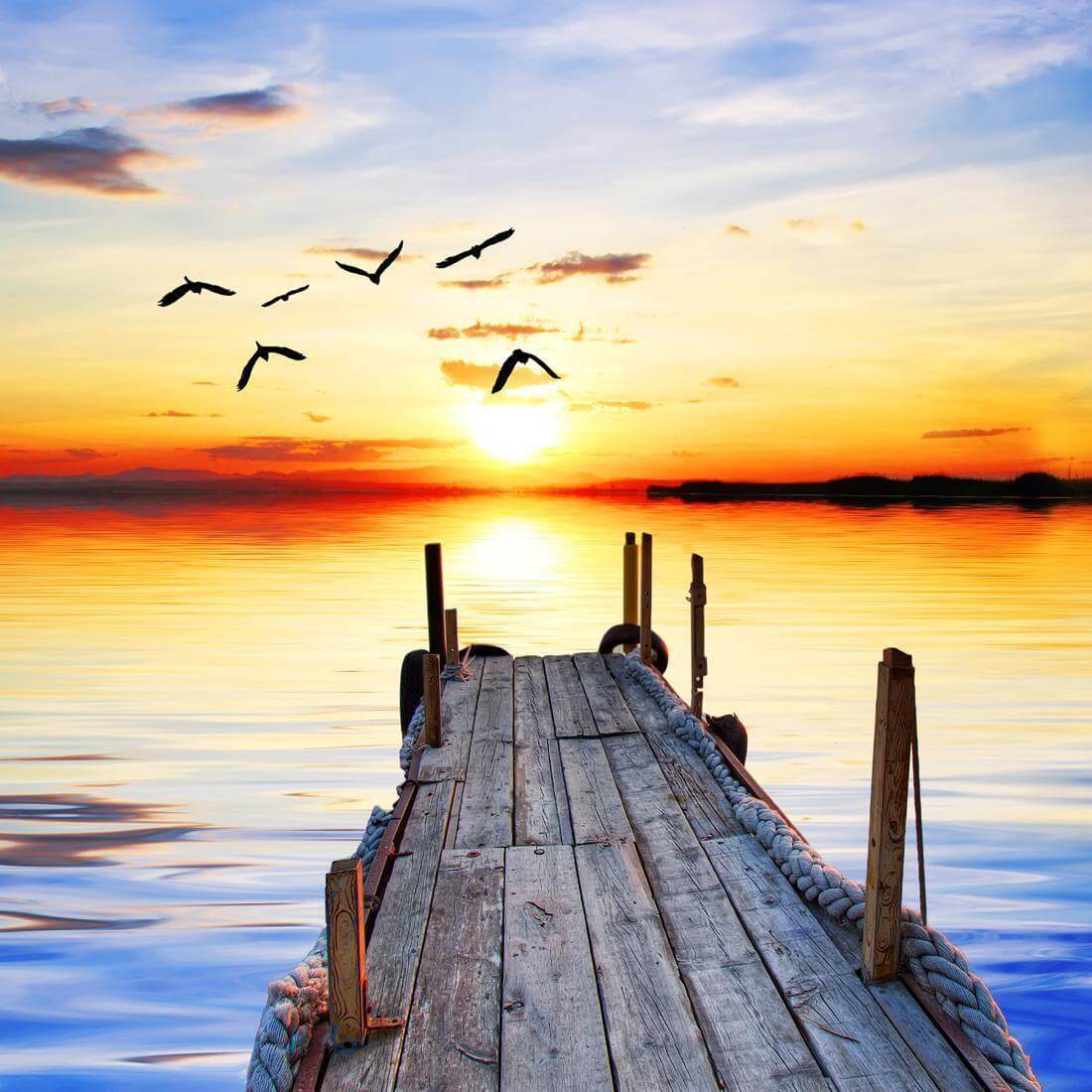 Stretched canvas wall art of an abandoned jetty at sunset with birds flying over calm waters.